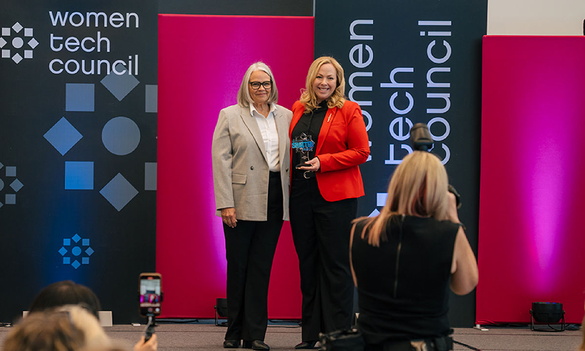 A woman takes a photo of Gloria Pitt and Sarah Teofilo, who is holding an award. 